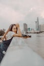 A Vietnamese girl standing by the riverbank admiring the view of Ho Chi Minh city with Bitexco Financial Tower, many buildings and