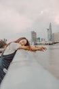 A Vietnamese girl standing by the riverbank admiring the view of Ho Chi Minh city with Bitexco Financial Tower, many buildings and