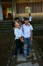 Vietnamese little boy pupils wear uniform: white t shirt, blue trousers standing on flooded school yard front of poor building