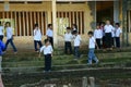 Vietnamese little boy pupils wear uniform: white t shirt, blue trousers standing on flooded school yard front of poor building