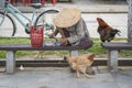 Vietnamese old woman in a straw hat sits on a bench and eats food on a street in the old city in Hoi An, Vietnam