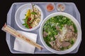 Vietnamese street food, pho bo soup with greens and rice flour noodles, plastic tray served with a large bowl of soup Hanoi street Royalty Free Stock Photo