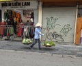 Vietnamese street vendor in Hanoi, with bamboo frame over shoulder carrying two big baskets of vegetables for sale Royalty Free Stock Photo
