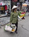 Vietnamese street vendor in Hanoi, walking across a street carrying flowers to sell in each hand Royalty Free Stock Photo