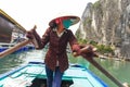 Vietnamese woman rowing boats that bring tourists traveling inside limestone cave with limestone island in background in summer.