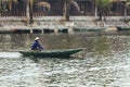 Vietnamese woman wearing blue long arm t-shirt, mask and conical hat rowing a boat on the river at Trang An Grottoes in Ninh Binh