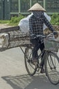 Vietnamese woman wearing a conical hat rides a bike carrying the metal frame of a bed matress Royalty Free Stock Photo