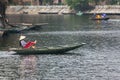 Vietnamese woman wearing purple long arm t-shirt conical hat rowing boat by her feet on the river at Trang An Grottoes.