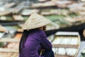 Vietnamese woman wearing purple long arm t-shirt conical hat siting and waiting on the land for tourist at Trang An Grottoes.