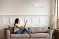 Vietnamese woman switching on air conditioner while resting seated indoors Royalty Free Stock Photo