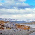 View of an abandoned house and mountains from an island covered by brown and orange vegetation on the Beagle Channel