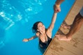 View from above of attractive girl in the swimming pool holding a man`s hand trying to get out at resort