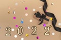 View from above. Beige background with star confetti, gift box with black ribbon and golden numbers. Happy new year 2022 greeting Royalty Free Stock Photo