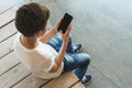 View from above. Boy in white T-shirt and sunglasses sitting indoor and uses smartphone. Teenager plays computer games Royalty Free Stock Photo