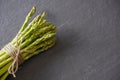 View from above of a bundle of green asparagus from above tied with twine on a gray slate counter with copy space