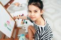 View from above of a creative little girl kid smiling, looking at the camera during painting on paper on an easel at home. A happy Royalty Free Stock Photo