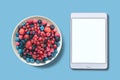 View from above. Different berries in a plate. Near the tablet with an assorted white screen. Royalty Free Stock Photo