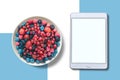 View from above. Different berries in a plate. Near the tablet with an assorted white screen. Royalty Free Stock Photo