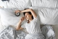 View from above. The girl sleeps next to the alarm clock. Trying to turn off the ringing alarm clock that interferes with sleep. Royalty Free Stock Photo