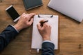 Top view of male hands writing something in a blank letterhead pinned to a clipboard. Businessman working at the table