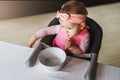 View from above. Nine-month-old baby girl in pink bandage sits at white table in highchair and eats herself with spoon from bowl Royalty Free Stock Photo