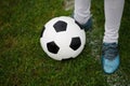 A classic football ball and feet of a young boy on a field background. Children training soccer. A ball on a grass. Royalty Free Stock Photo