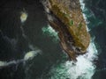 View from above. A small stone island covered with green moss in the middle of the ocean. Turquoise ocean water and white foamy Royalty Free Stock Photo