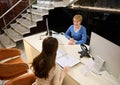 View from above to pleasant mature European woman retail manager, consultant sitting at reception desk in modern office building Royalty Free Stock Photo