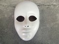 View from above of a white mask over a cracked gray surface. Royalty Free Stock Photo