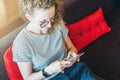 View from above. Young woman in glasses and a striped T-shirt is sitting at home on the couch and is using a smartphone. Royalty Free Stock Photo