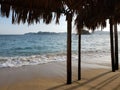 view of Acapulco beach from a palapa with palm roof and wooden supports on a sunny day Royalty Free Stock Photo