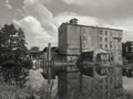 View accros Jizera river on abandoned, aged, dirty, empty industrial factory building in sepia tone, dramatic clouds and tree