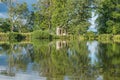 A view across a beautiful lake with reflections of trees towards an old abandoned structure in the middle of a rural countryside