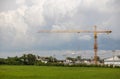 A view across a green rice field to a yellow crane installed on a construction site Royalty Free Stock Photo