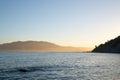 View across Tokomaru Bay in late afternoon as sun illuminates distant hills in golden glow