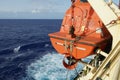 View on the aft part of orange colour lifeboat secured with davits and safety hooks on the container cargo vessel.