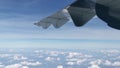 The view from an airplane window with the airplane wing, the cloud, and the blue sky scenery.