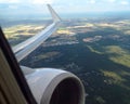 View through an airplane window to the wing and the jet engine over an agricultural landscape, travel concept