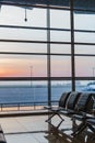 View of airport interoir, empty bench chairs in the departure hall during sunrise. Airplane and building background