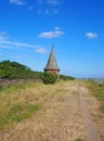 View along country straight lane with a stone wall at the side with an old pointed roofed building with a weather vane on a su