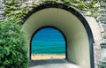 View through an arched gate to a bright beach with unrecognizable people and blue sea, daydream, composition