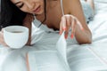 View of asian woman lying on bed, reading book and holding cup of tea Royalty Free Stock Photo