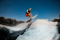 View of athletic man on surf style wakeboard jumping over splashing wave