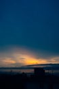 View on atmospheric sunset in blue, yellow and orange tones over sea and dark silhouettes of residential buildings. vertical Royalty Free Stock Photo