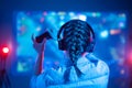 View from back of beautiful gamer woman playing video game at home in front of big screen with joystick and headphone. Colorful