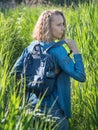 A view from the back of a blonde woman in a denim dress takes off his backpack on a path in the tall grass. Travelling in wild Royalty Free Stock Photo