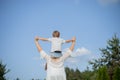 View from back, boy is sitting on his mother's shoulders, their hands are joined against blue sky. Royalty Free Stock Photo