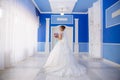 View from the back The bride in a wedding dress with a long lace train goes around the room with high ceilings and blue Royalty Free Stock Photo