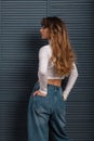View from the back on a fashionable slender young woman with long chic red hair in fashion youth clothes near wooden curtains in