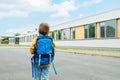 A view from the back of a girl with a school bag on her back is standing next to the school building. Beginning of the